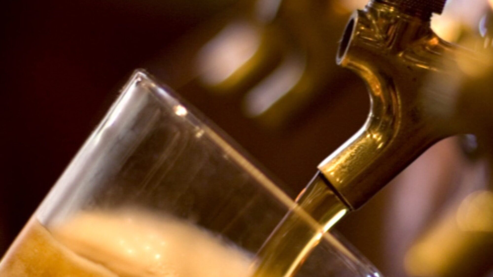 A close-up of a beer tap pouring beer into a tilted glass, with foam forming at the top.