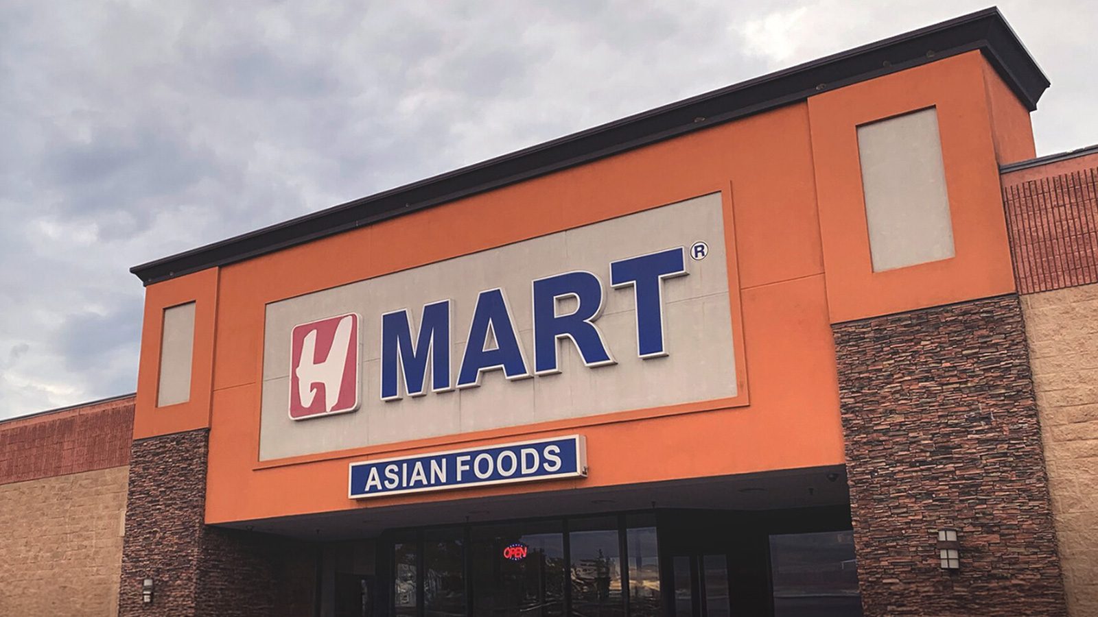 The storefront of H Mart, an Asian foods market in Ballard, boasts an orange and brick facade under a cloudy sky.