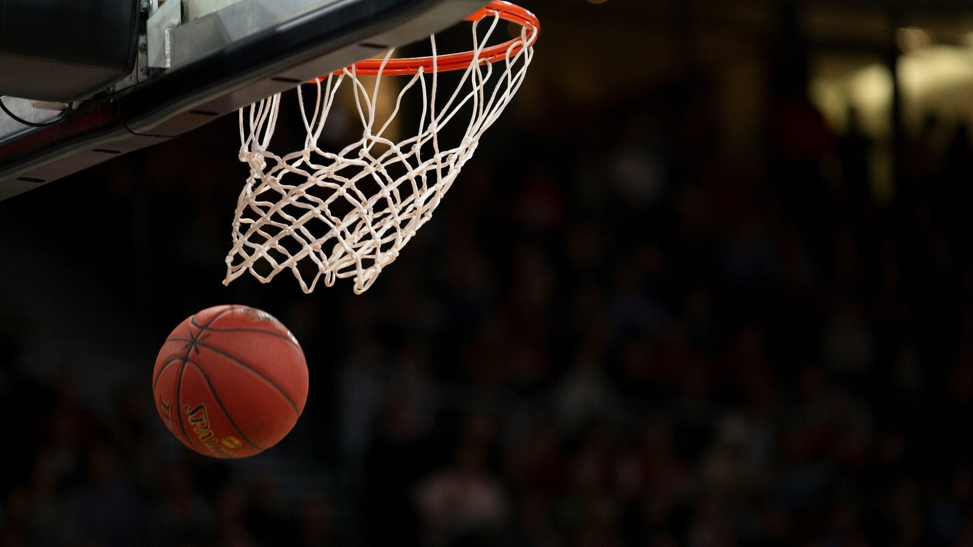 During March Madness, a basketball arcs towards the hoop, with an electrified crowd visible in the background.