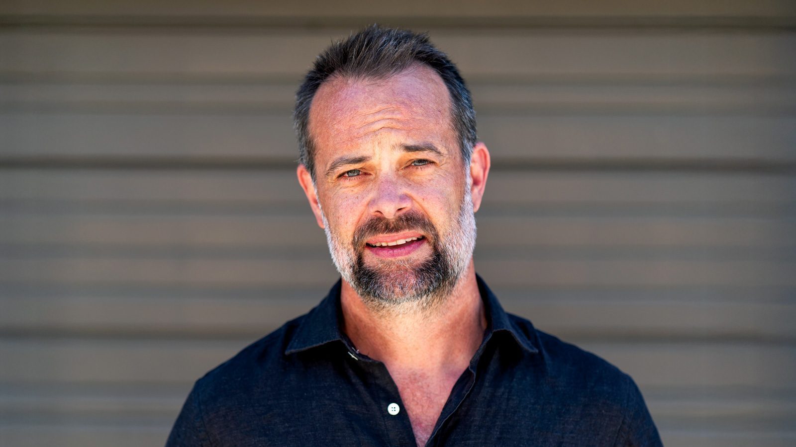 A man with a beard and short hair stands confidently in front of a blurred striped background, reflecting the innovative spirit of a Seattle ad agency. He's dressed in a dark shirt, gazing directly at the camera.