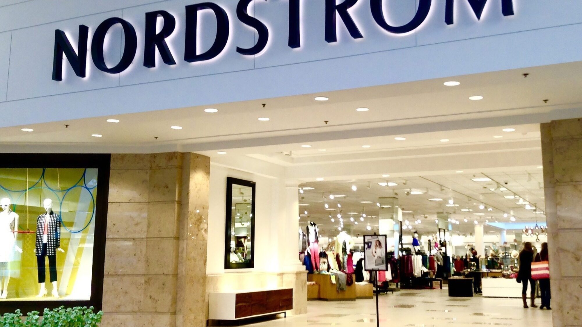 Entrance of a Nordstrom department store with clothing displays and mannequins visible inside.