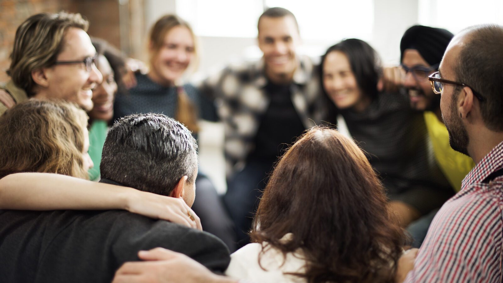 A diverse group of people are sitting close together in a circle, smiling and embracing each other, suggesting unity and camaraderie, reflecting a positive organizational culture.