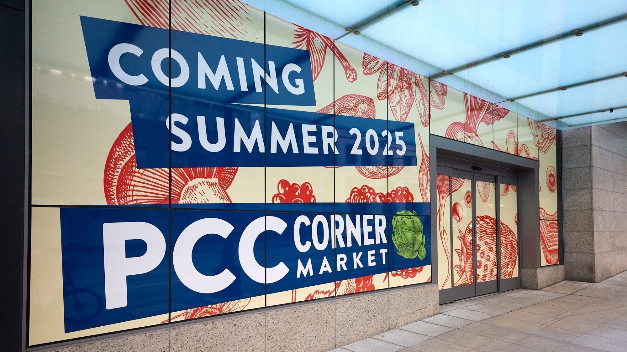 Storefront displays a large sign reading "Coming Summer 2015 PCC Corner Market" with fruits and vegetables illustrated in the background.