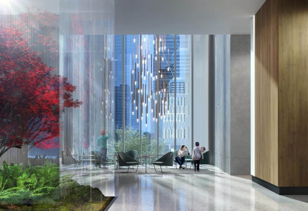 Modern lobby with tall glass walls, red-leaved tree, and hanging light installations. Three people are seated at a table, and one person is standing near the glass. City buildings are visible outside, hinting at a future Health Hub where wellness meets innovation.